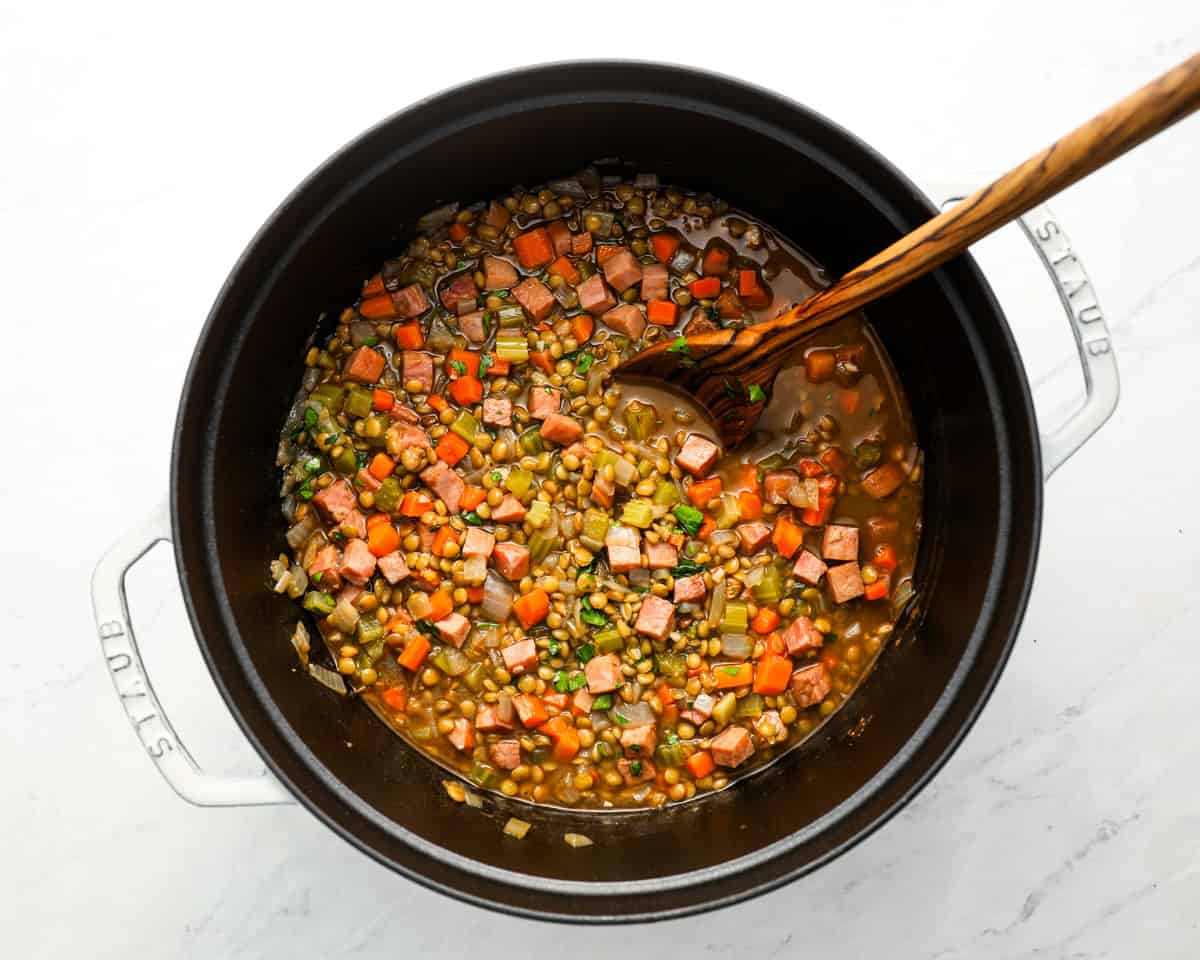 Ham and lentil soup in a Dutch oven, now thickened and fully cooked with a wooden spoon resting inside.