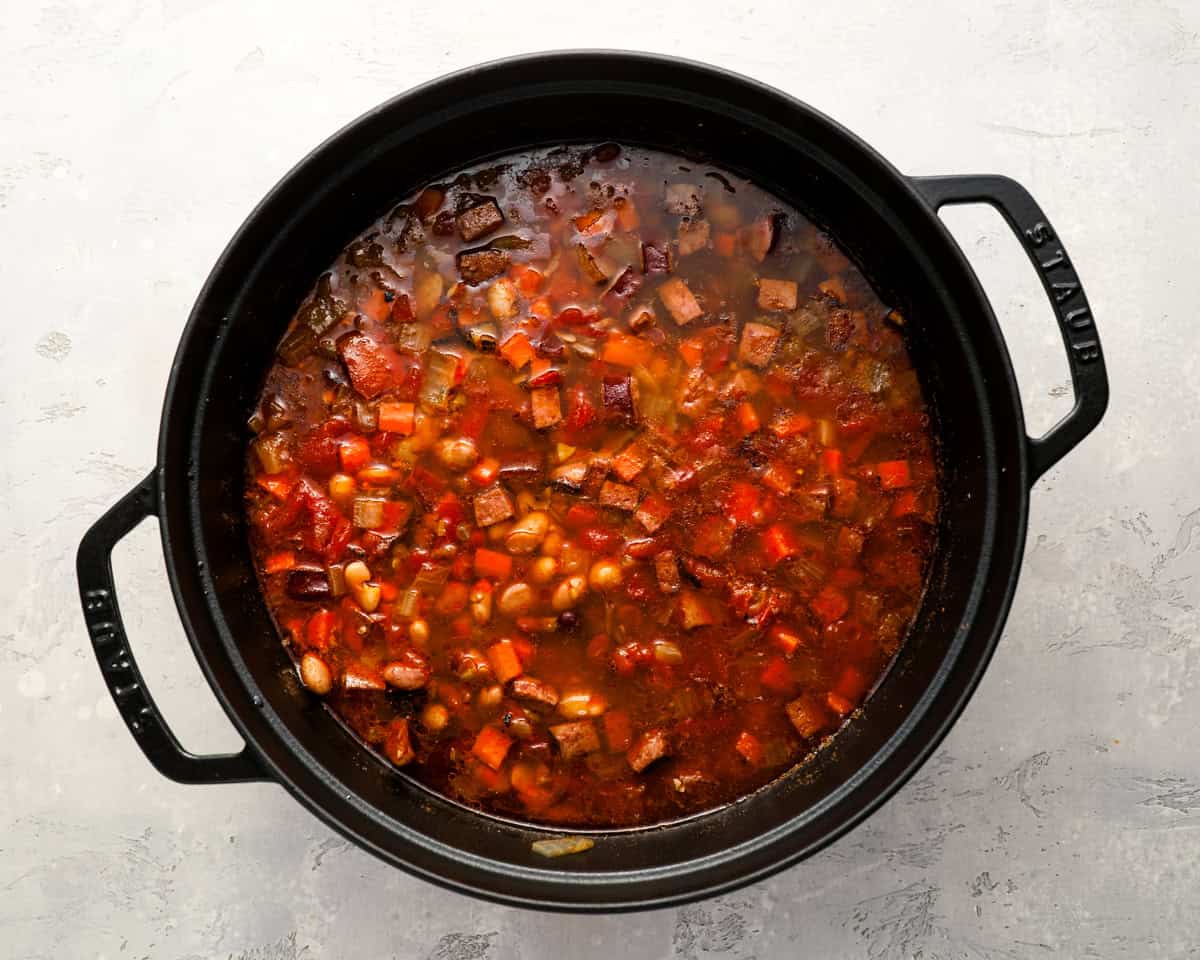 A Dutch oven filled with thickened 15 bean soup, packed with visible chunks of tomato, beans, carrots, and sausage.