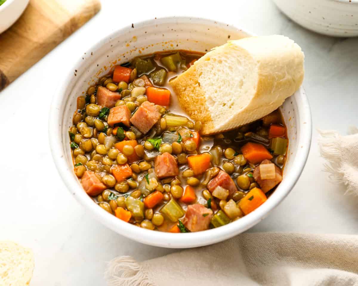 Another close-up of the soup bowl with crusty bread resting on the edge, highlighting the hearty texture of the soup.