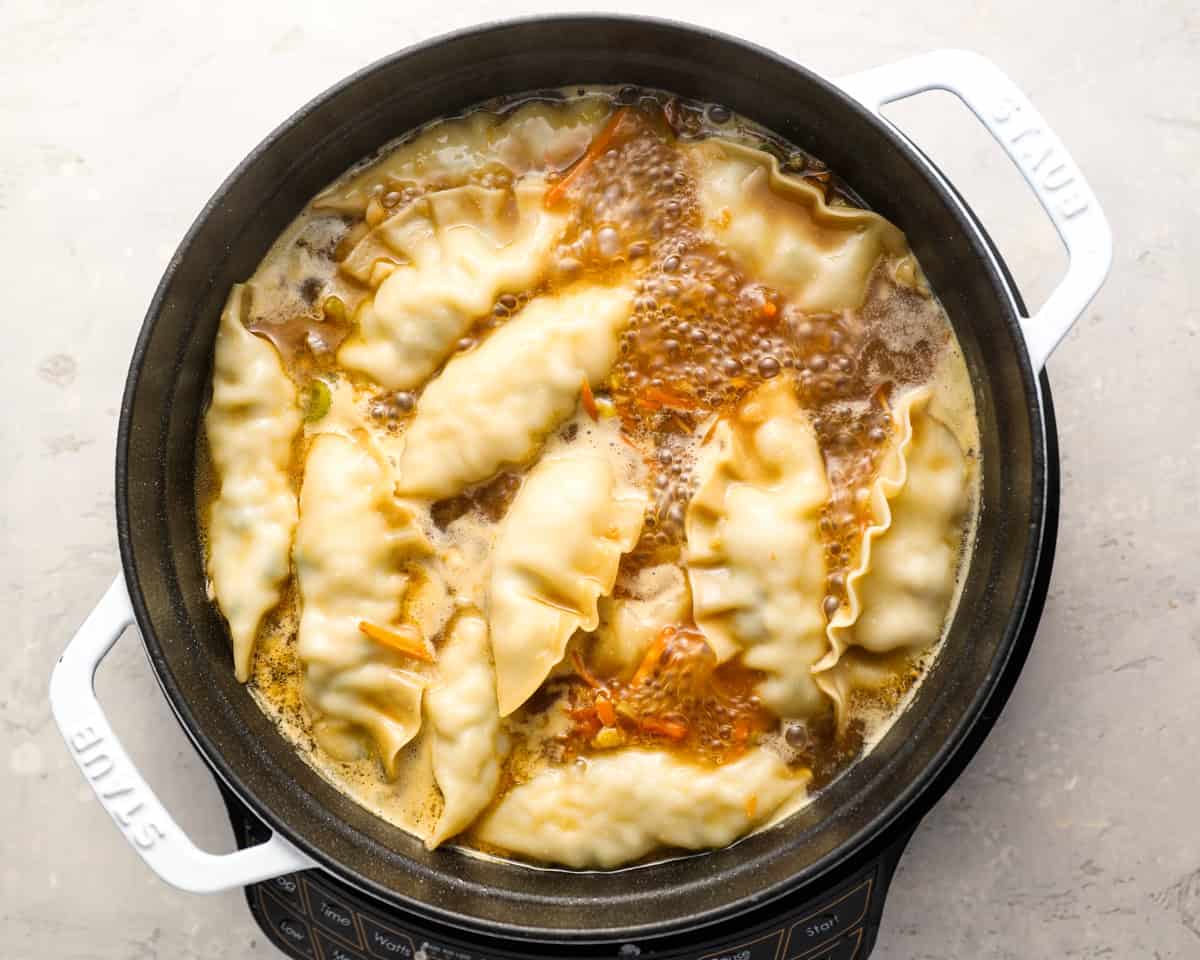 Dumplings cooking in boiling broth inside a Dutch oven, partially submerged.