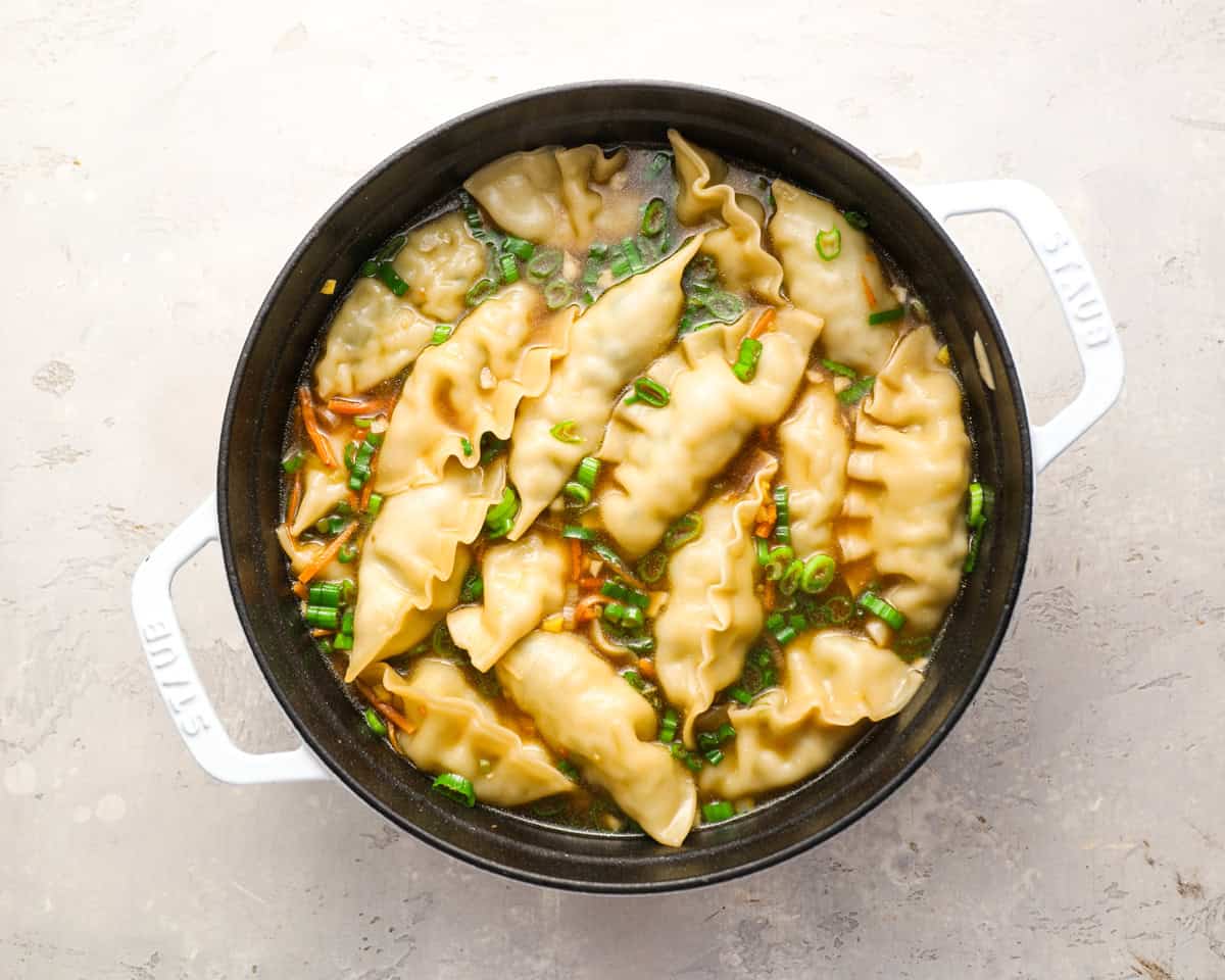 Fully cooked dumplings floating in a rich broth with carrots and scallions.