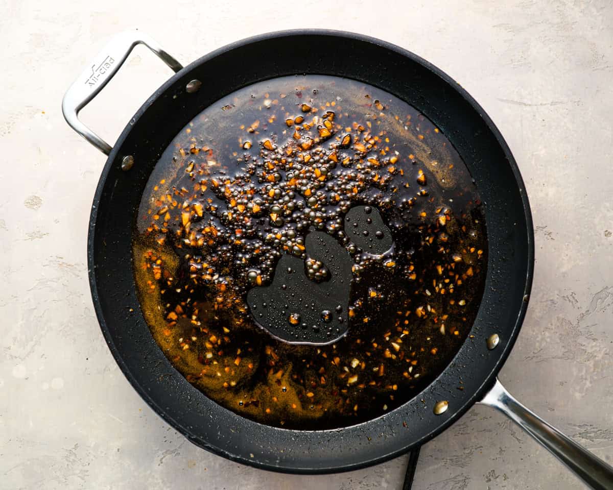 Honey garlic sauce with garlic and red pepper flakes simmering in a skillet.