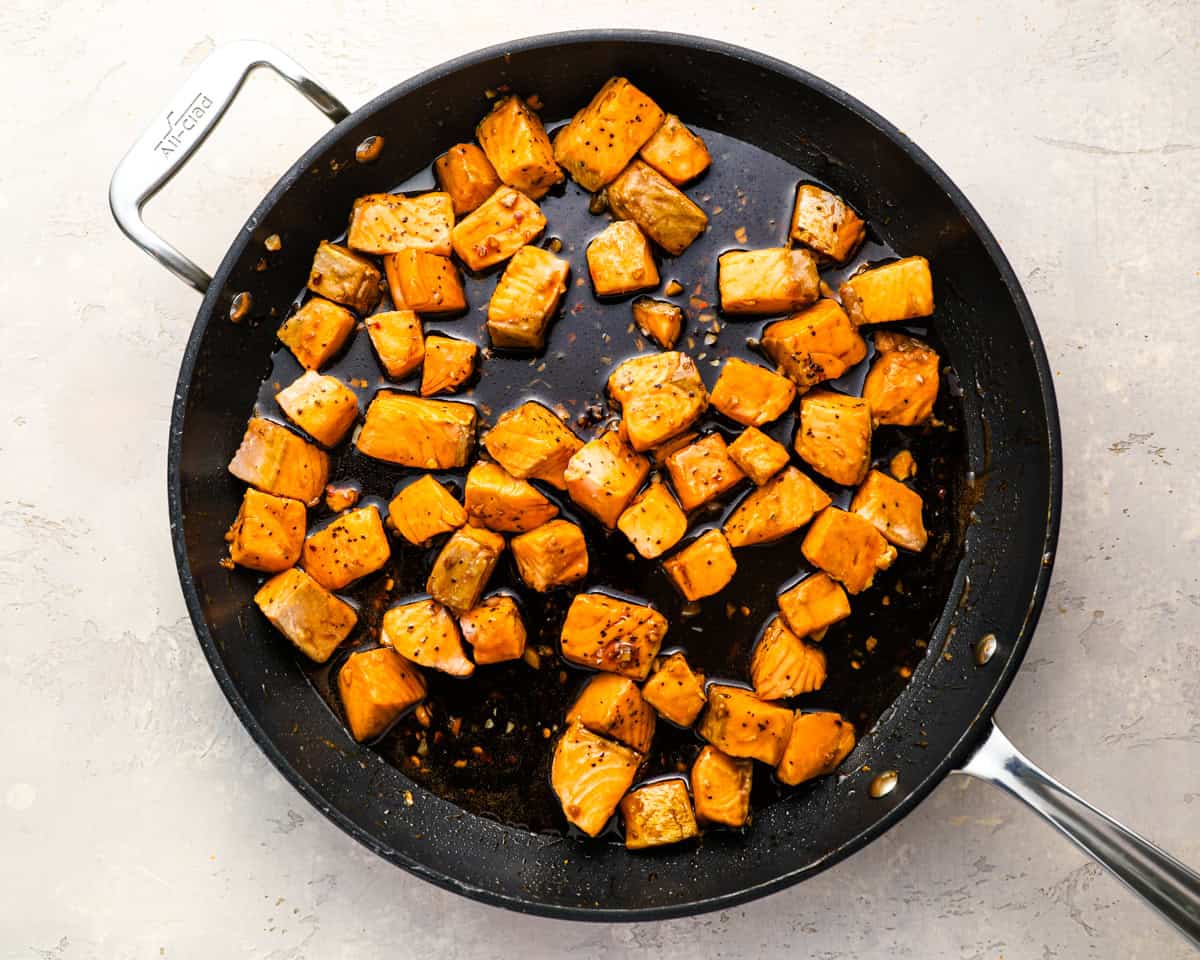 Cooked salmon cubes tossed in honey garlic sauce in a skillet.