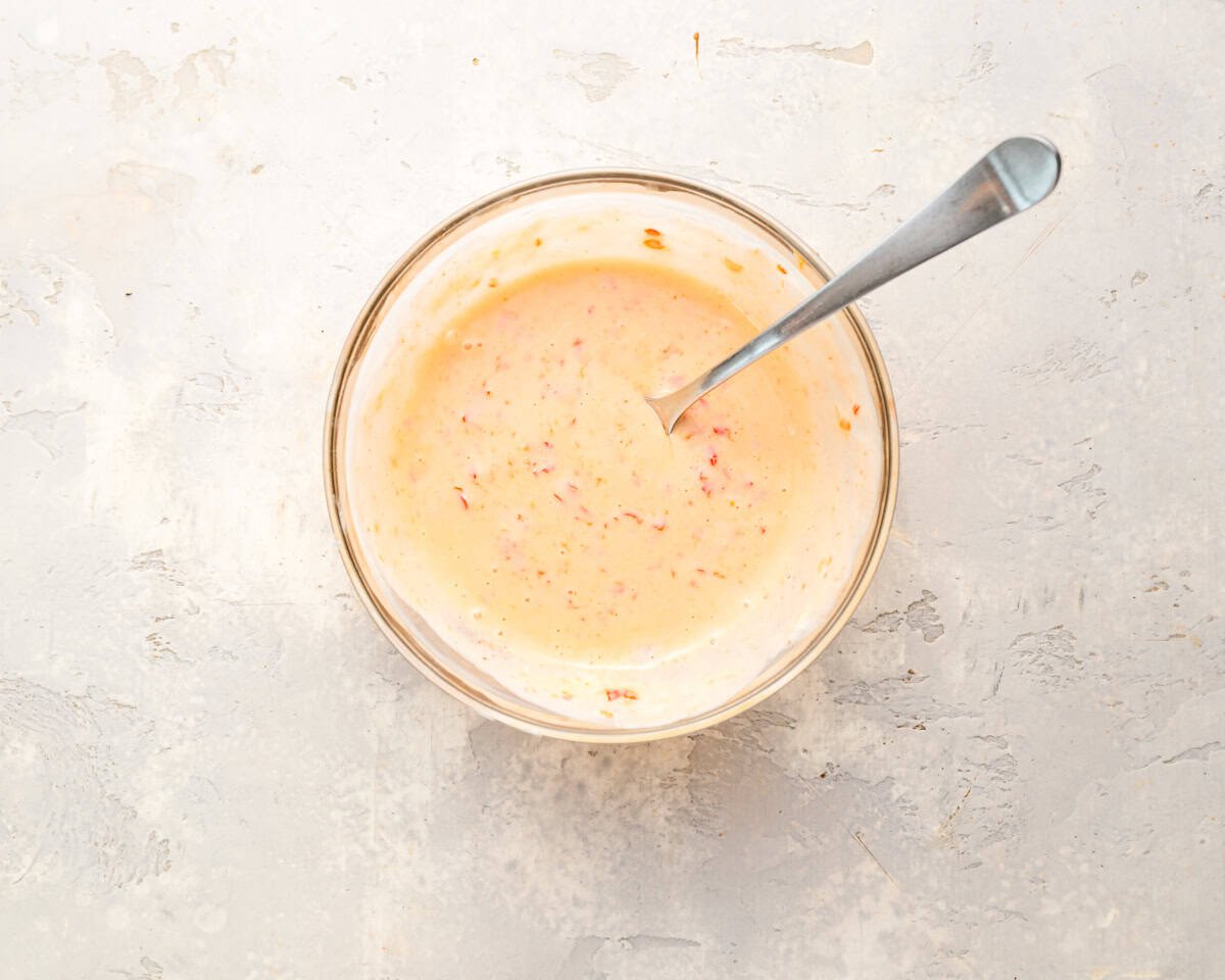 Creamy Bang Bang sauce made with yogurt, sweet chili sauce, and sriracha in a glass bowl with a spoon.