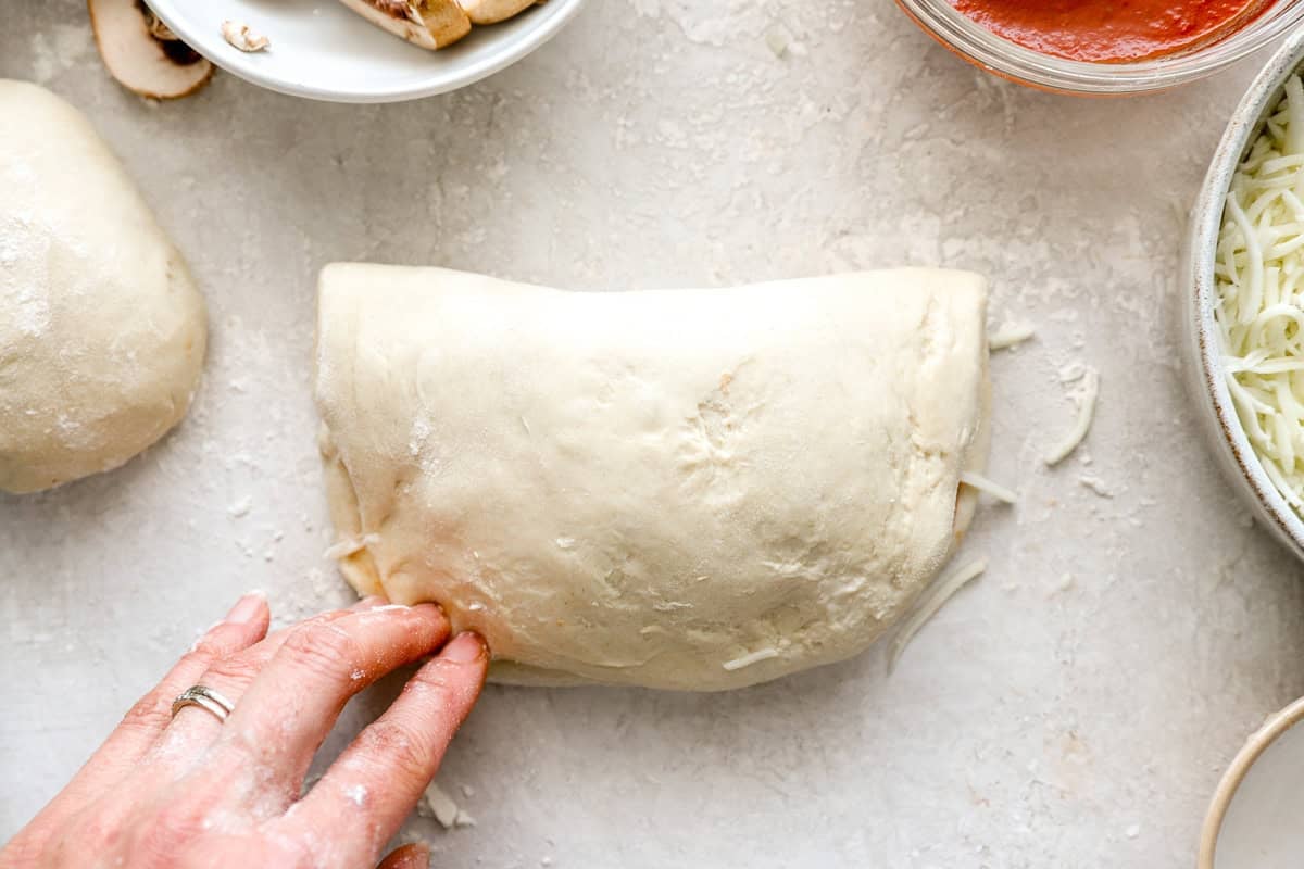 Dough folded over fillings to form a calzone, with edges being sealed by hand.