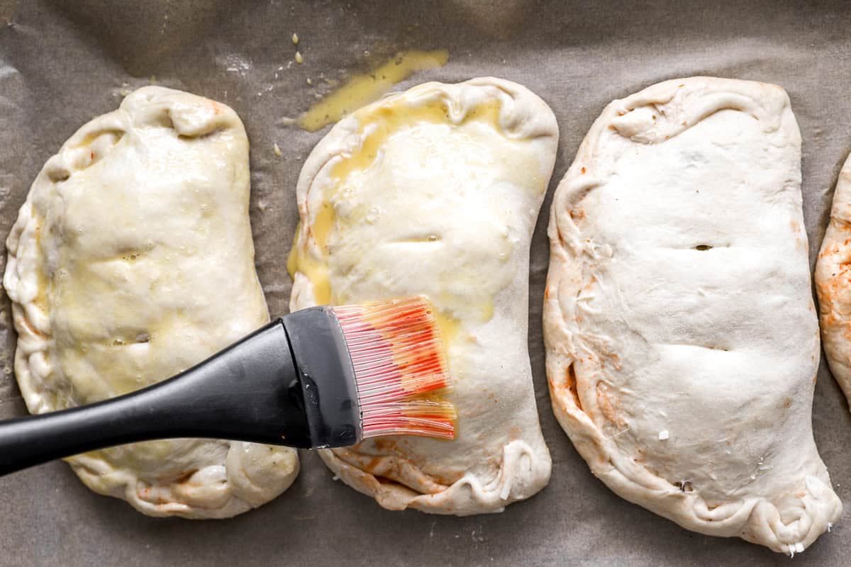 Egg wash being brushed onto calzones before baking to give them a golden finish
