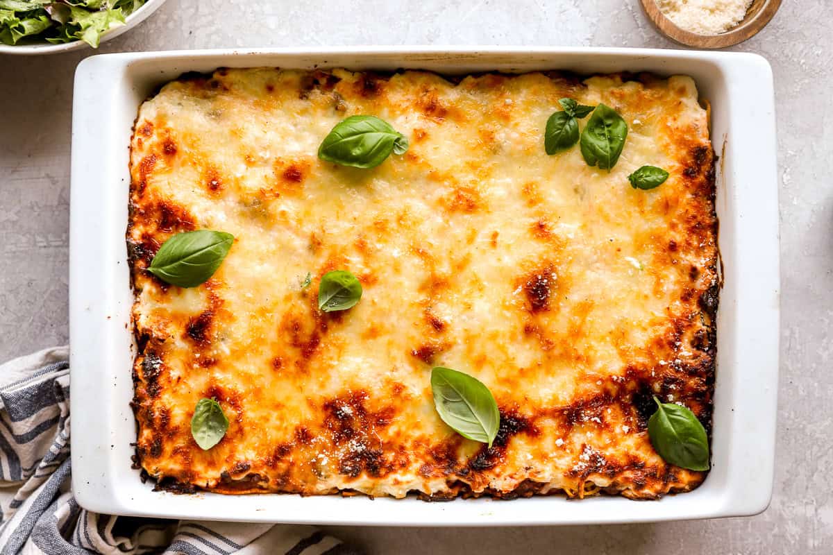 Fully baked million dollar spaghetti casserole with golden, bubbly mozzarella cheese and fresh basil on top.