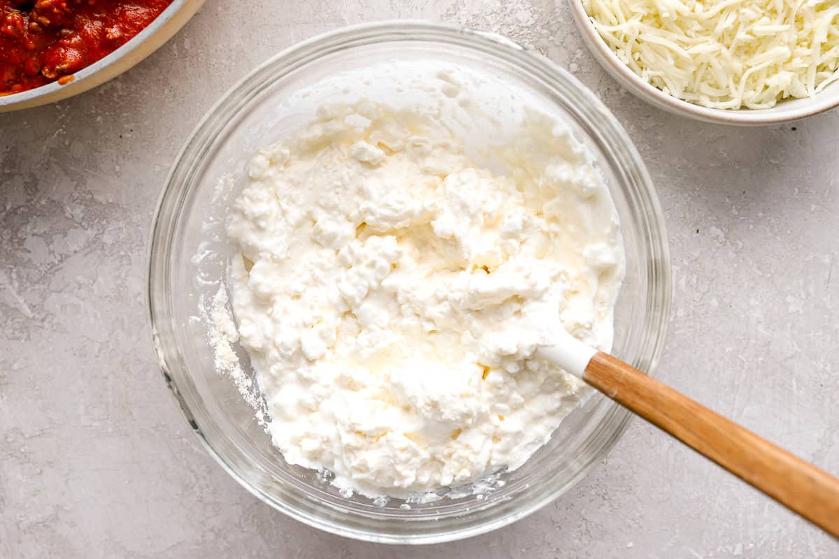 Creamy cheese mixture made from cottage cheese, sour cream, and cream cheese in a mixing bowl with a spatula.