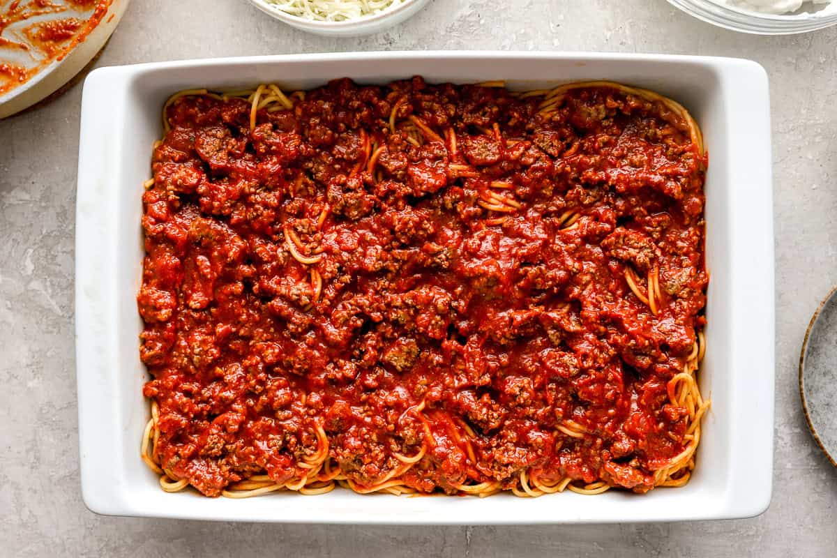 Spaghetti topped with meat sauce layered in a white casserole dish, ready for the next step in assembly
