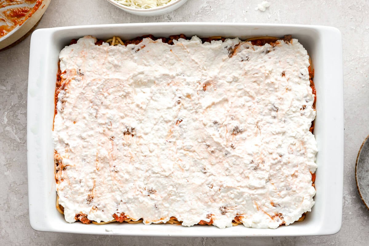 Creamy cheese layer spread evenly over the meat and spaghetti in a white casserole dish.
