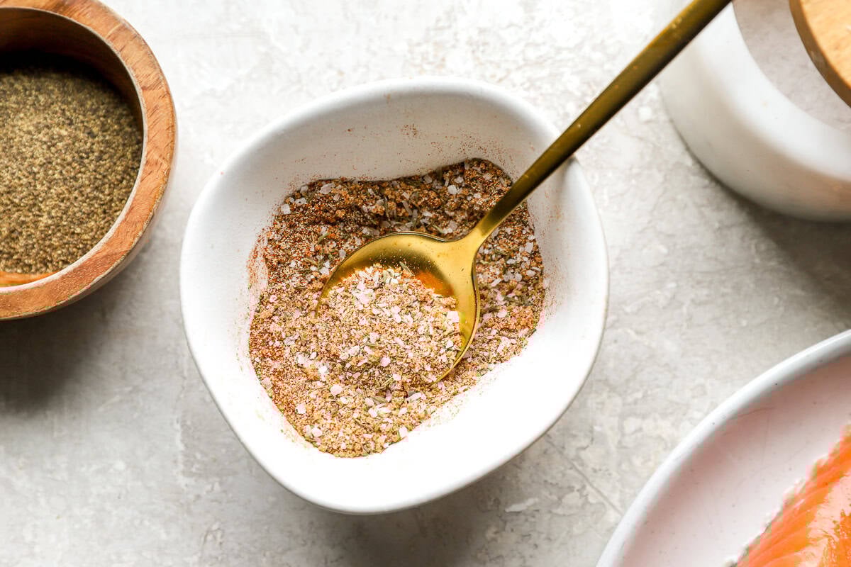A white bowl filled with a coarse salmon seasoning blend and a gold spoon scooping it up.