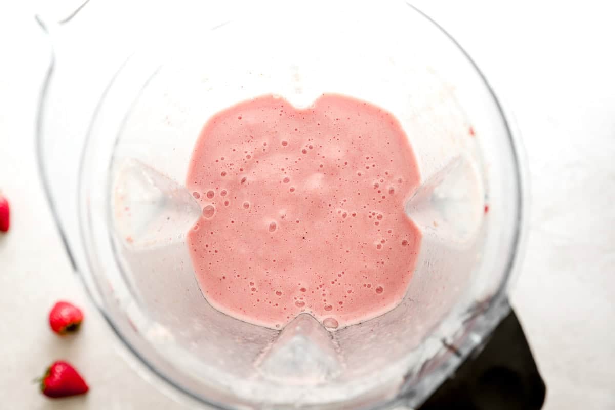 Blended strawberry banana smoothie inside a blender, showing the creamy pink texture from above.