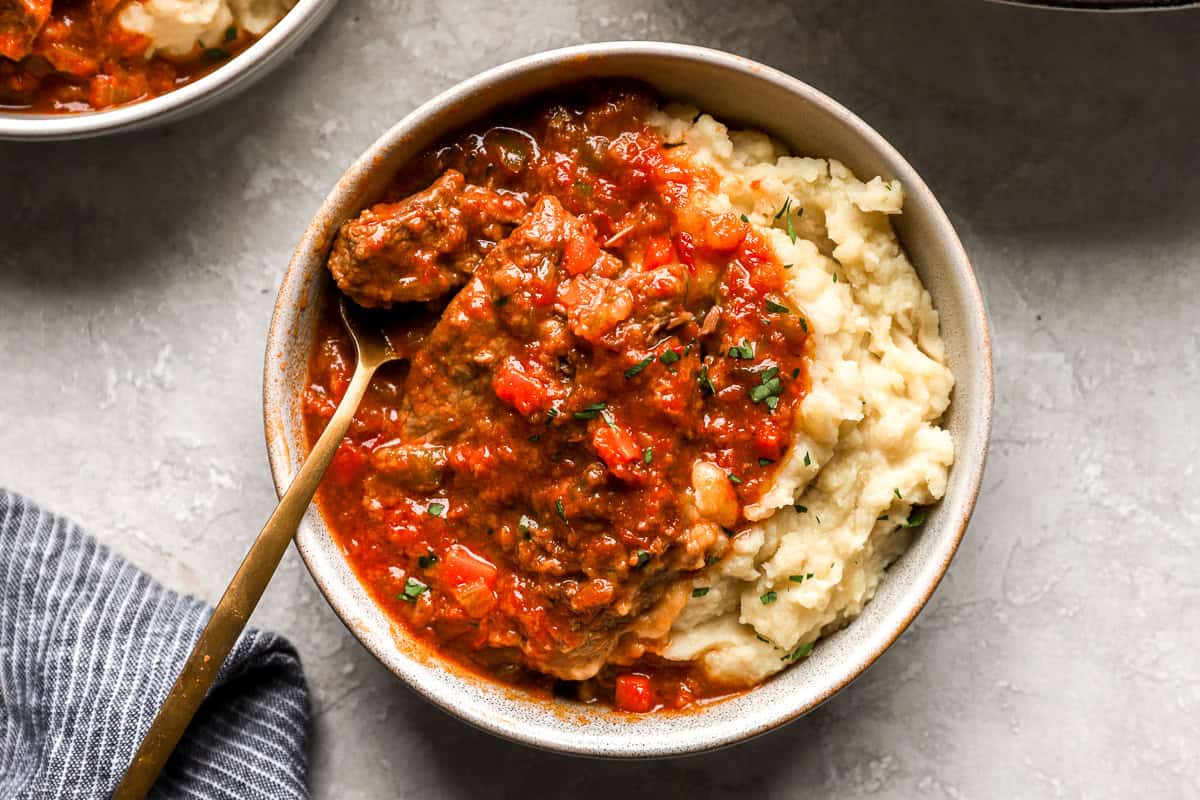 Overhead view of a bowl filled with mashed potatoes and Swiss steak in tomato sauce, ready to be served with a spoon.