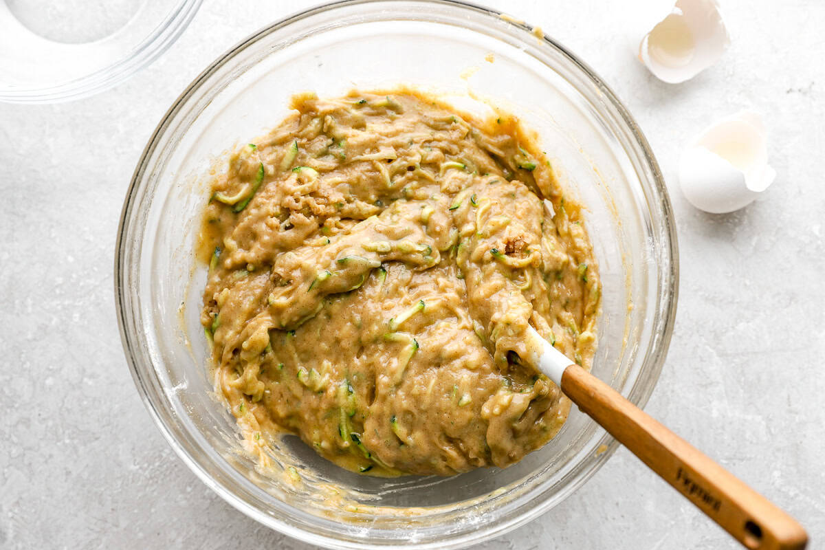 Thick zucchini bread batter in a glass mixing bowl, folded together with a rubber spatula.