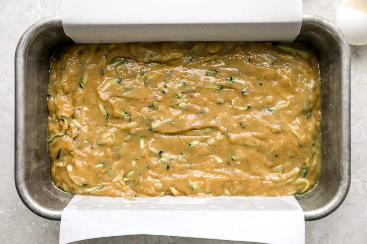Zucchini bread batter poured into a parchment-lined loaf pan, ready to go into the oven.