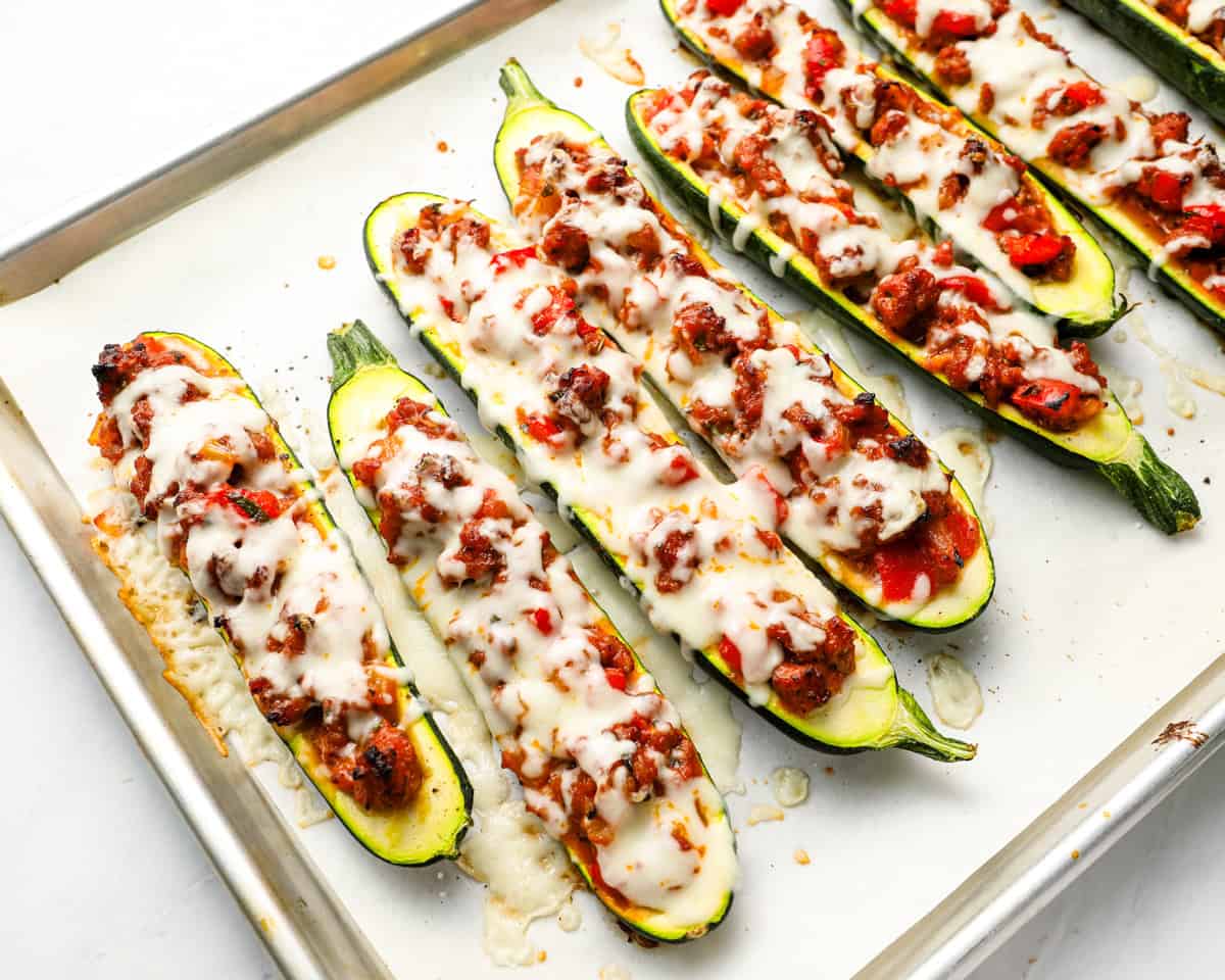 Close-up of cheesy baked stuffed zucchini boats on a parchment-lined baking tray.