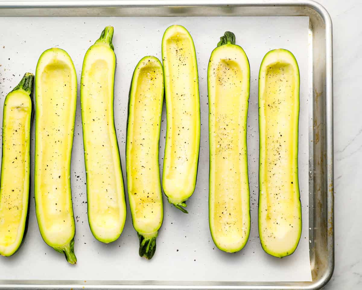 Zucchini boats placed on a parchment-lined baking sheet, lightly seasoned with salt and pepper.