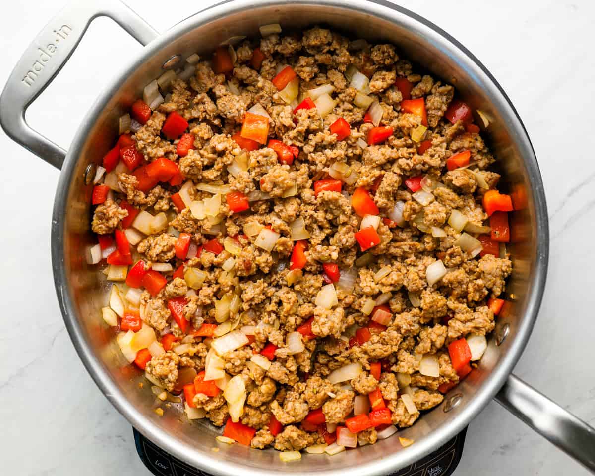 Ground Italian sausage, red bell pepper, and onion sautéing in a large stainless steel skillet.