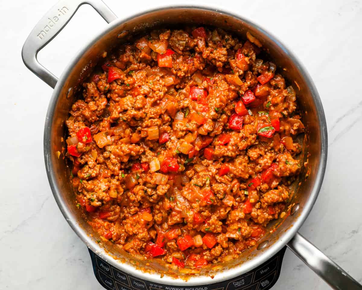 Fully cooked sausage filling in the skillet with tomato sauce and chopped basil mixed in.