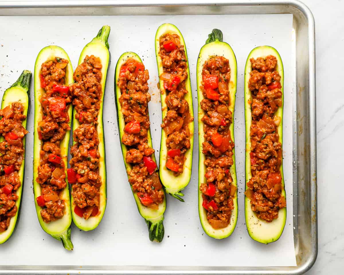 Zucchini boats filled with sausage mixture arranged on a baking sheet, ready to go in the oven.