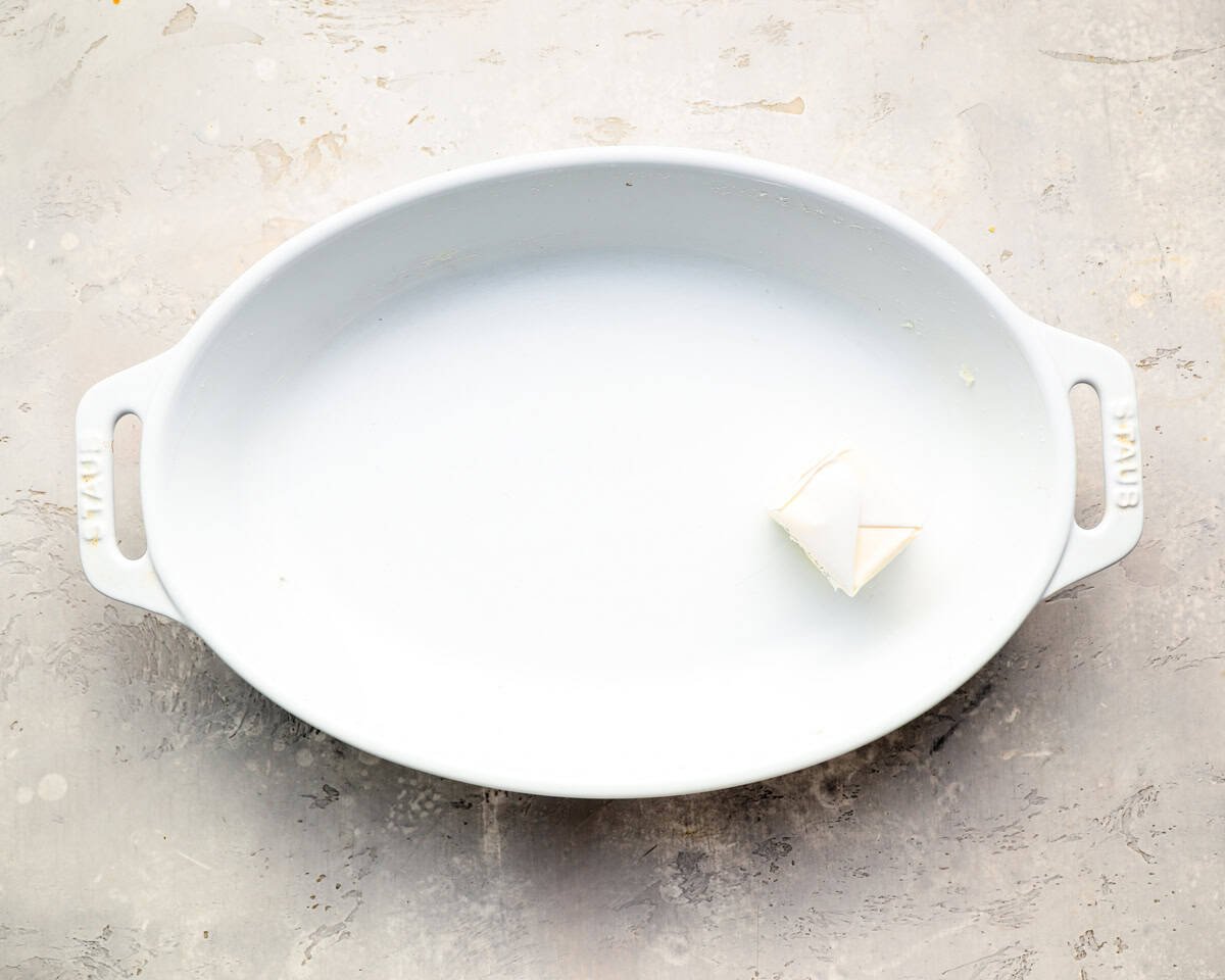 White oval baking dish with a pat of butter placed in the center, ready to be greased.