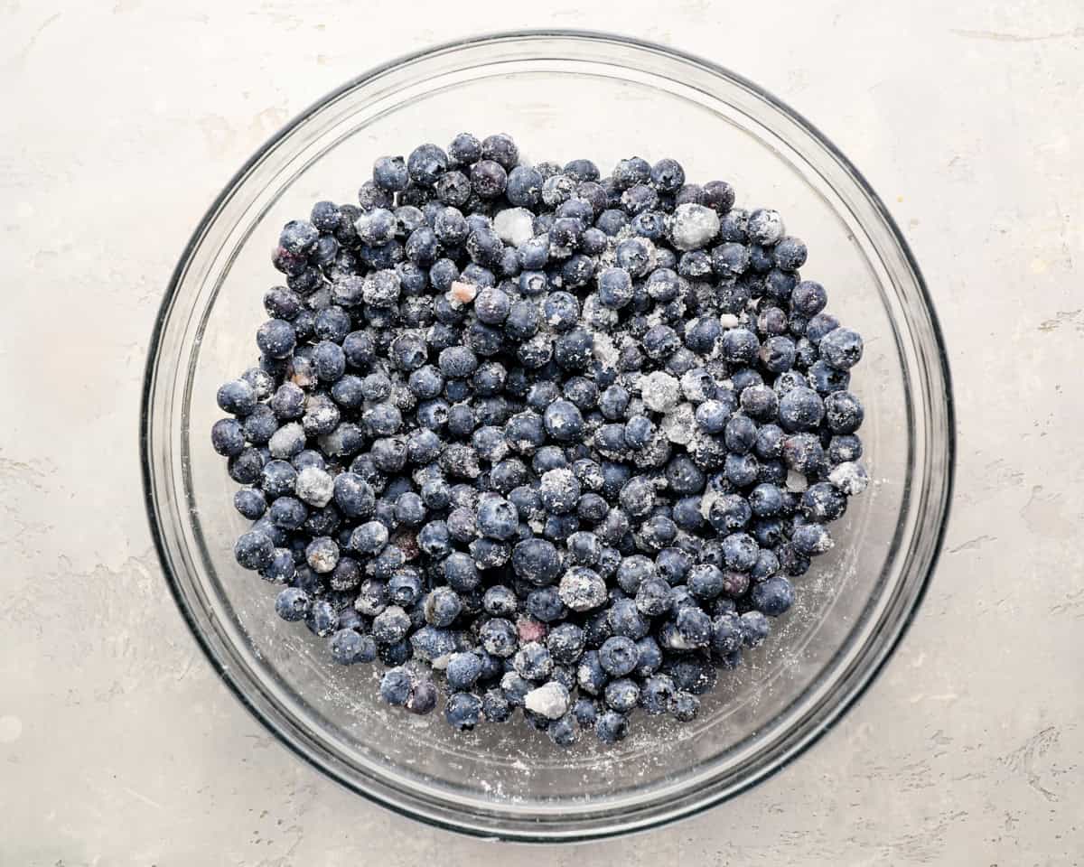 Glass mixing bowl filled with fresh or frozen blueberries tossed with sugar and cornstarch.