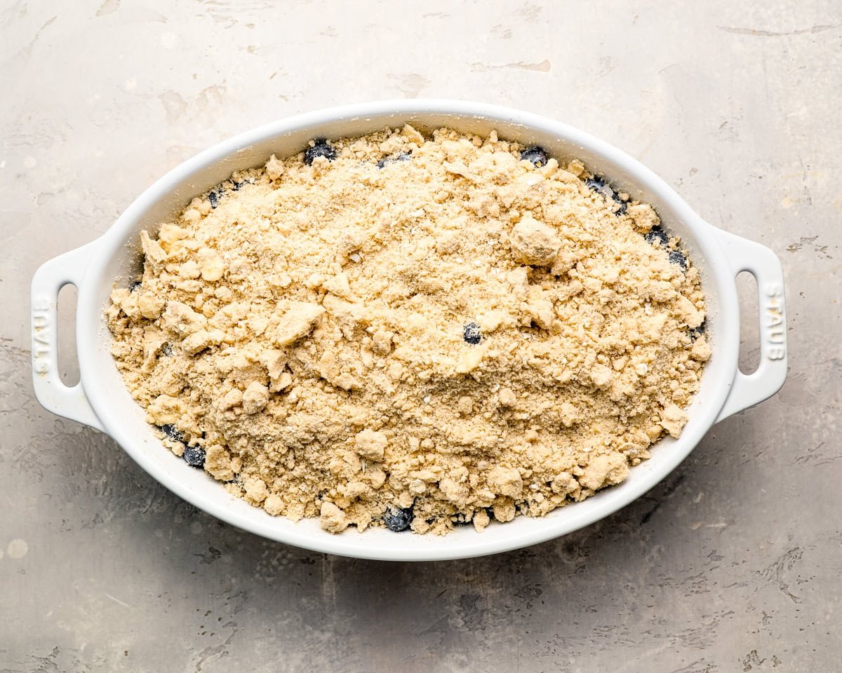 Baking dish with the crisp topping sprinkled over the blueberry filling, ready to go into the oven.