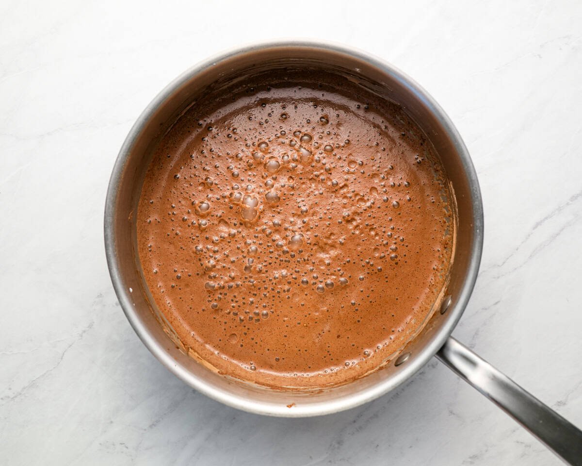 Chocolate pudding mixture starting to bubble as it thickens on the stovetop in a saucepan.