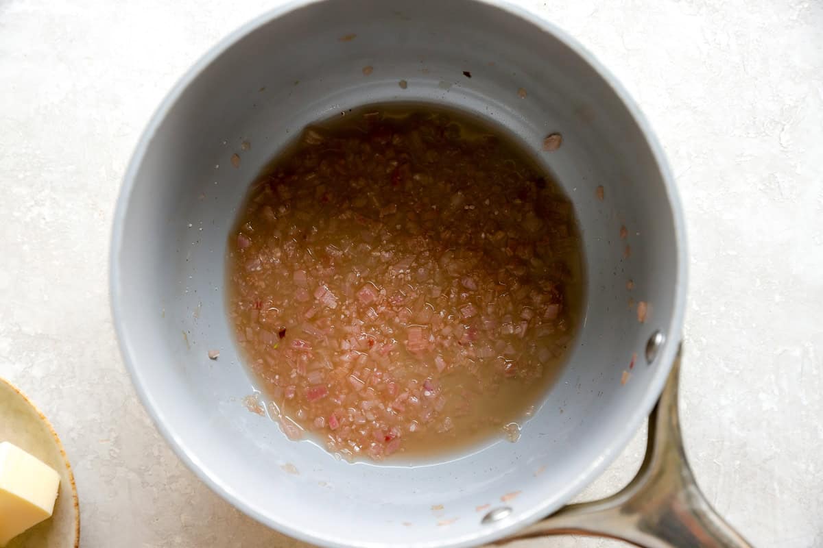 Shallots simmering in wine and vinegar in a saucepan as the first step in making beurre blanc.