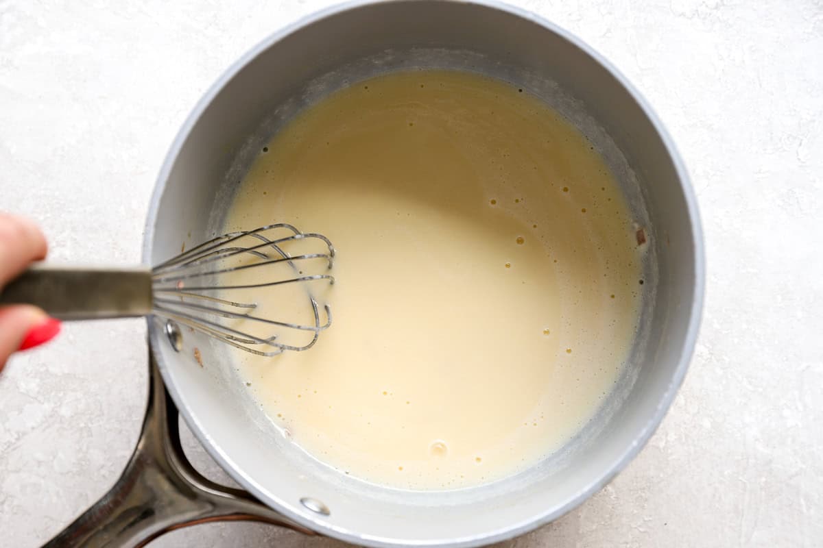 Finished beurre blanc sauce being whisked to a smooth consistency in a saucepan.