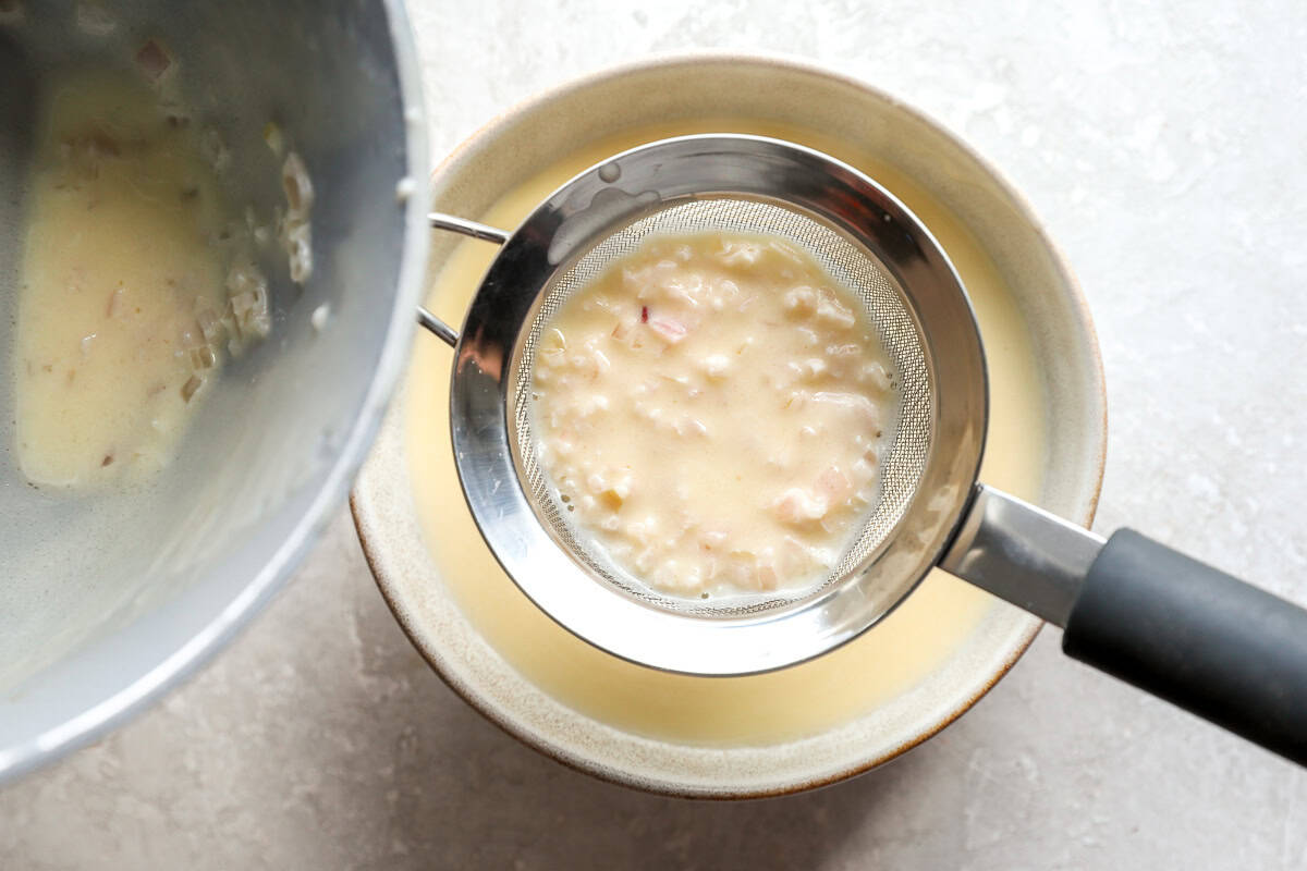 Pouring beurre blanc sauce through a fine mesh strainer to remove shallots.