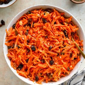 Overhead view of a large white bowl filled with carrot raisin salad served with a gold spoon.