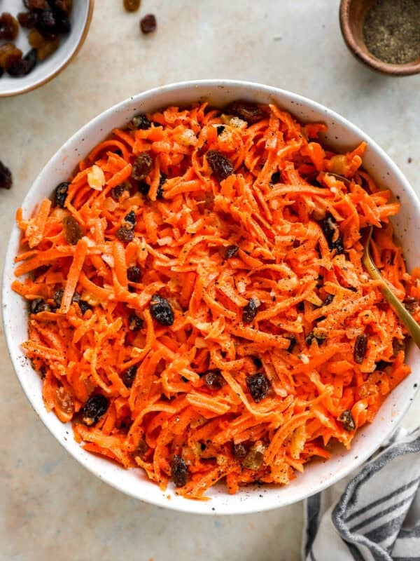 Overhead view of a large white bowl filled with carrot raisin salad served with a gold spoon.