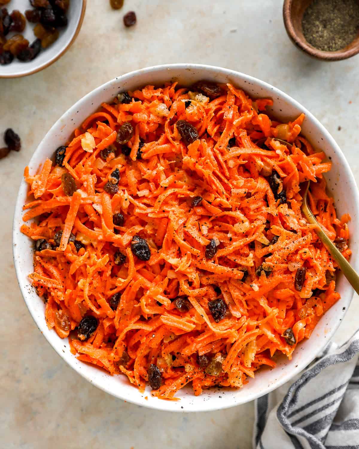 Overhead view of a large white bowl filled with carrot raisin salad served with a gold spoon.