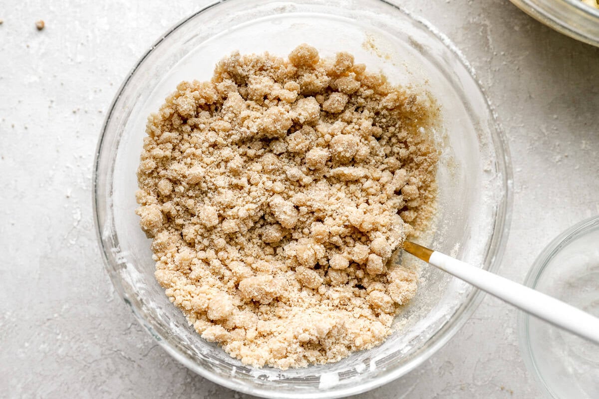 Bowl of crumble topping mixture with a spoon, showing buttery, clumpy texture before baking.