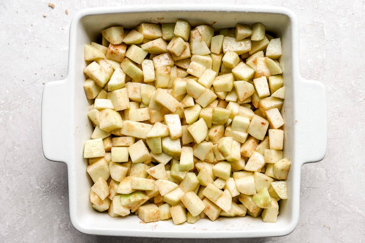 White square baking dish filled with seasoned apple pieces before adding the topping.