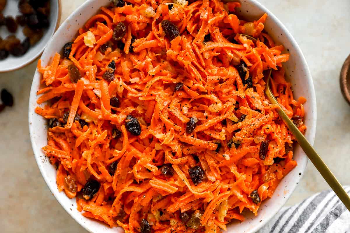 Close-up overhead view of carrot raisin salad in a white bowl, with raisins and pineapple mixed throughout.