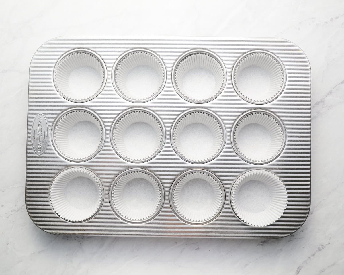 Silver muffin tin filled with white cupcake liners.