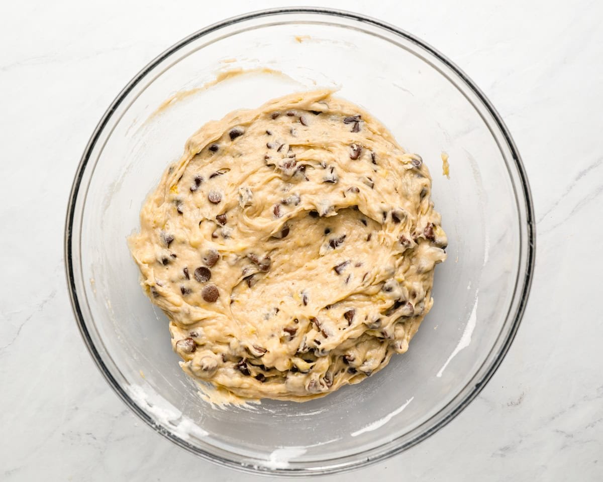 Banana chocolate chip muffin batter fully mixed in a clear glass mixing bowl.