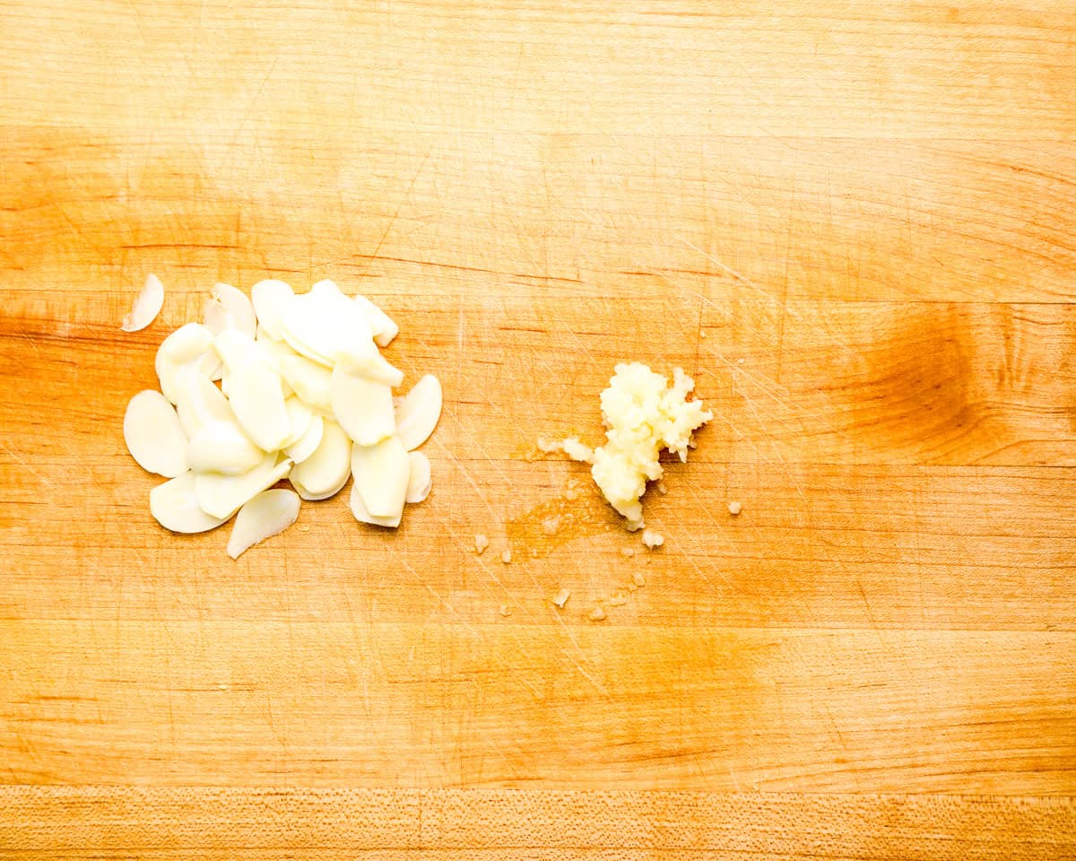 Sliced and grated garlic on a wooden cutting board.