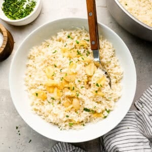 Overhead view of garlic rice served in a white bowl, garnished with crispy toasted garlic and chopped parsley