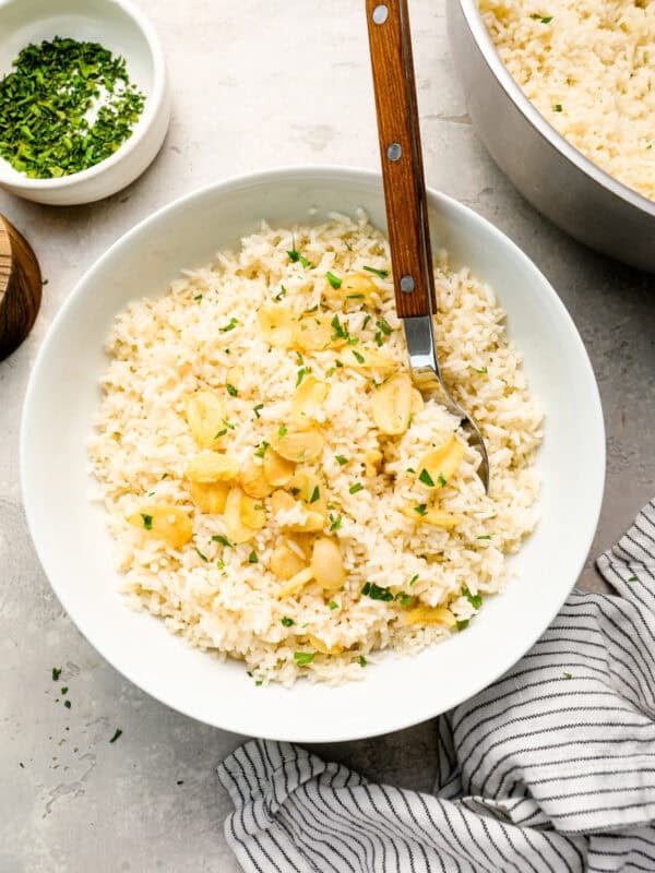 Overhead view of garlic rice served in a white bowl, garnished with crispy toasted garlic and chopped parsley