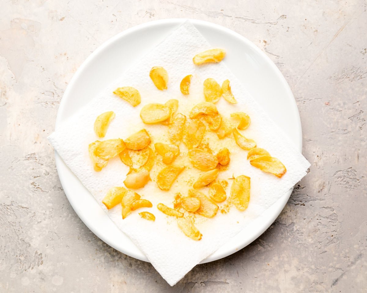 Sliced, fried garlic on a paper-towel lined white plate.