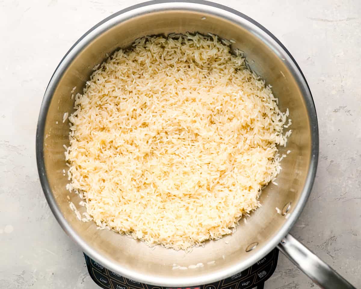 Uncooked white rice being toasted in a stainless steel skillet on a light gray textured surface