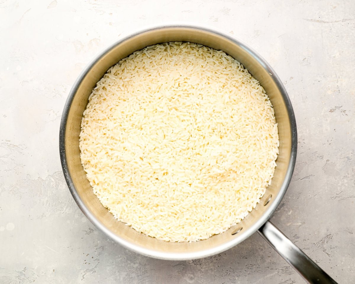 Fluffy, cooked garlic rice in a stainless steel skillet on a light gray textured surface
