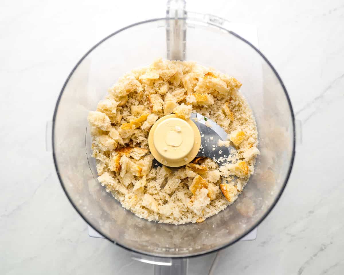 Food processor filled with torn pieces of crusty bread, ready to be pulsed into breadcrumbs.
