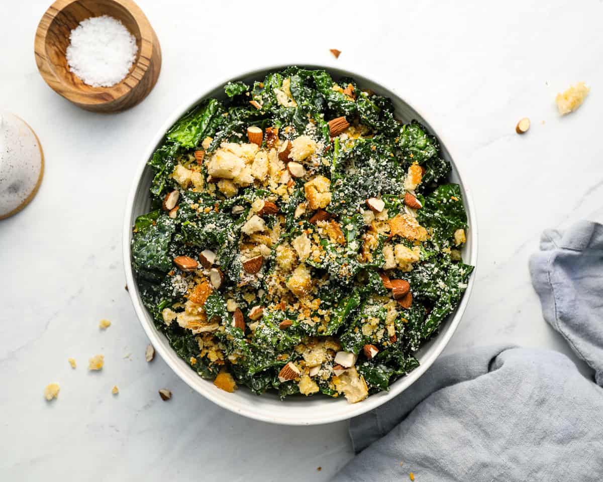 Finished kale salad in a serving bowl, garnished with almonds, parmesan, and crispy breadcrumbs.