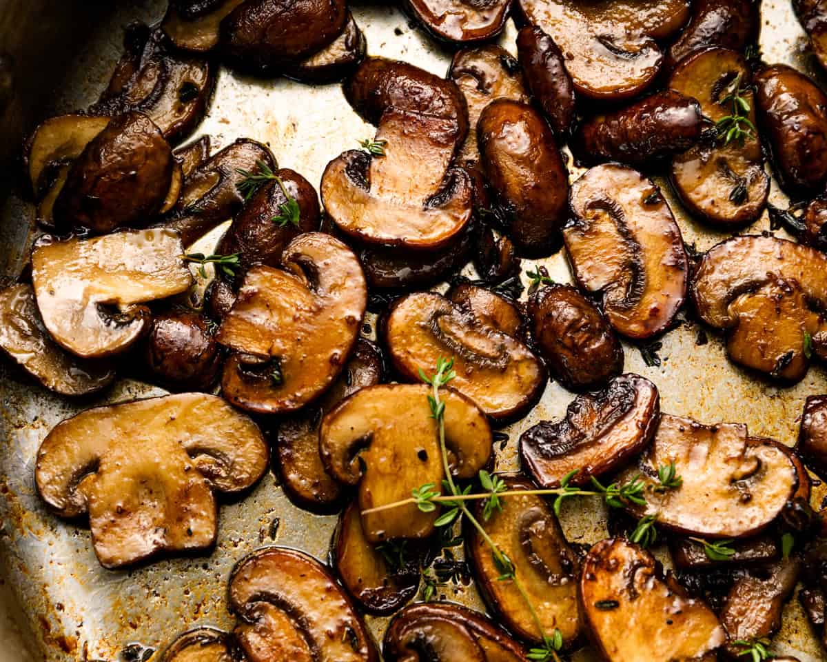 Close-up of golden-brown sautéed mushrooms in a skillet with sprigs of thyme scattered throughout.
