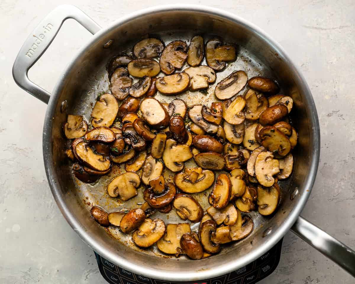 Mushrooms partially browned in a stainless steel skillet, starting to develop golden edges and reduce in volume.