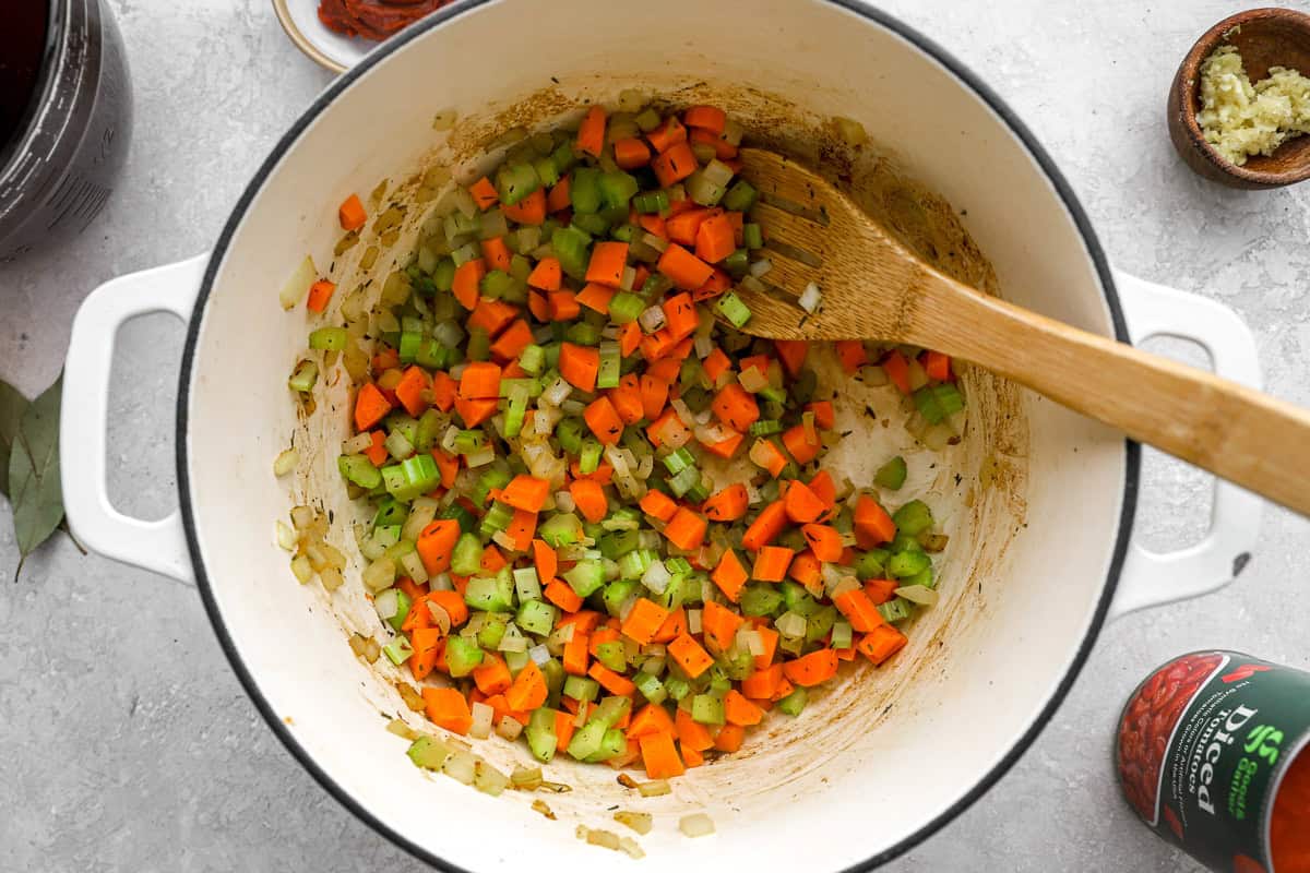 Chopped carrots, celery, and onions sautéing in a Dutch oven with a wooden spoon, building the flavor base for the soup.